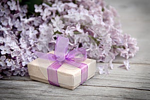 Gift box with purple bow and lilac on wood