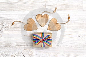 Gift box with rainbow LGBT ribbon and wooden hearts on a light wooden background