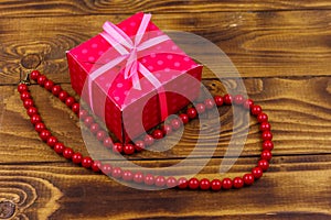 Gift box and red beads necklace on wooden background