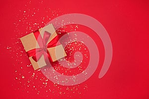 Gift box with red bow on bright red background with golden sparkles around and copyspace for your text. Festive backdrop