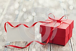 Gift box with red bow ribbon and empty paper note on table for Valentines day