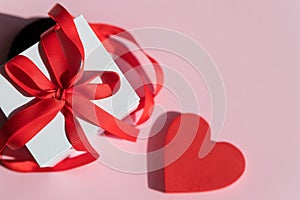 white Gift box with red bow ribbon and red heart on pink background for Valentines day.Happy birthday, wedding, greeting