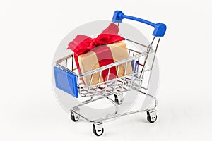 Gift box with a red bow and ribbon in a metal shiny shopping trolley on wheels on a white background