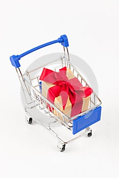 Gift box with a red bow and ribbon in a metal shiny shopping trolley on wheels on a white background
