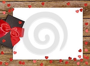 Gift box with red bow ribbon and paper heart on wooden background for Valentines day