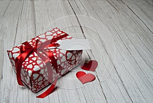 Gift box and red hearts on a light wooden background.
