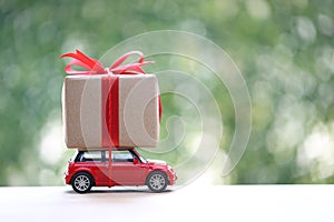 Gift box with red ribbon on miniature car on green background.