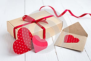 Gift box with a red ribbon  two red hearts  love letter on a white wooden background. Valentine\'s day background