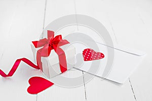 Gift box with a red ribbon  two red hearts  love letter on a white wooden background. Valentine's day background