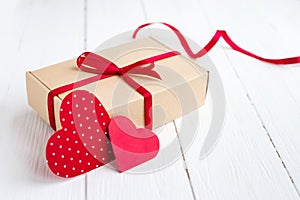 Gift box with a red ribbon  two red hearts on a white wooden background. Valentine\'s day background