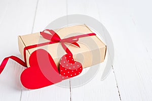 Gift box with a red ribbon  two red hearts on a white wooden background. Valentine's day background with copy space