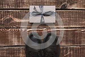 Gift box with ribbon and men`s leather shoes on a wooden background. Father`s day. Gift for a man.