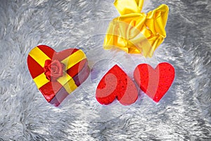 Gift box in the shape of a heart tied with a yellow ribbon with a bow in the shape of a rose lies on the pillow fake fur and next