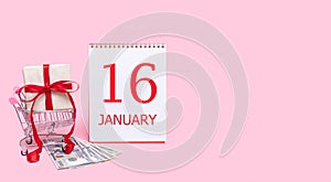 A gift box in a shopping trolley, dollars and a calendar with the date of 16 january on a pink background.