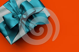 Gift box with turquoise ribbon on orange background