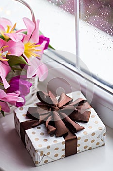 Gift box and tender bouquet of beautiful pink tulips in white basket near window with raindrops in the daylight