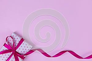 The gift box is tied with pink ribbon on a pink background. Concept for Valentine`s Day, Women`s Day, Birthday. Flat lay