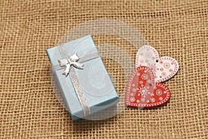 Gift box and two wooden hearts stand on burlap fabric