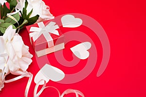 Gift box with white bow, flowers and heart on red background. Free space for your text