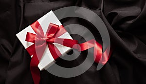 Gift box white with red ribbon on black satin. Christmas Valentine day present, black Friday