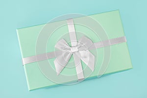 Gift box with a white silver bow, mint green on a mint turquoise background. Holiday gift minimal concept. Top view, flat lay,