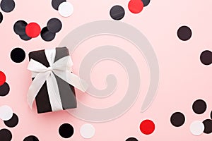 Gift box wrapped in black paper & white bow on pink background w