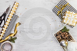 Gift box wrapped in black and white striped paper with golden ribbon, a crate full of pine cones and christmas toys and wrapping m