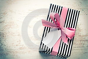 Gift box wrapped in black and white striped paper with pink ribbon on a white wood old background. Empty note tied over. Vintage