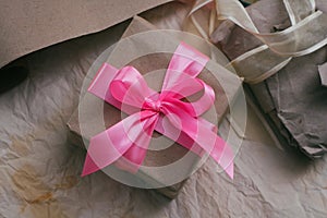 Gift box wrapped in brown craft paper and tied by pink satin ribbon. Packaging process. Gift shop. Wedding decor.