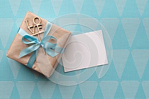 Gift box wrapped in brown paper with light blue ribbon on blue background with greeting card. Mockup. Freespace