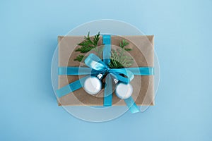 Gift box wrapped of craft paper, blue ribbon and decorated fir branches and silver Christmas balls on the blue background.