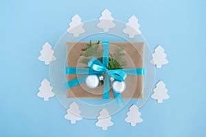 Gift box wrapped of craft paper, blue ribbon and decorated fir branches and silver Christmas balls on the blue background.