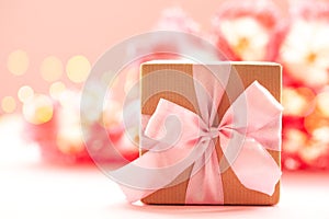 Gift box wrapped with craft paper and pink bow on pink flowers background photo