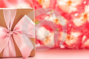 Gift box wrapped with craft paper and pink bow on pink flowers background