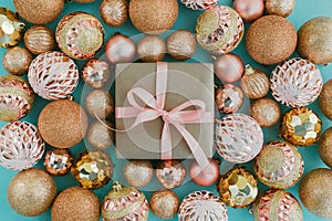 Gift box wrapped in craft paper with pink ribbon and golden Christmas tree balls on pale blue background with glitters