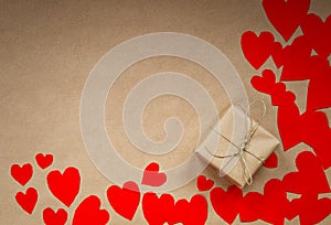 Gift box wrapped in kraft paper surrounded by red hearts on brown plain paper background, Valentines Day concept top
