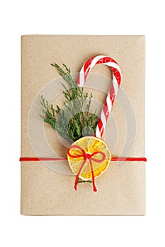 Gift box wrapped in kraft paper, tied with red twine and decorated with a juniper branch, orange slice and candy cane.