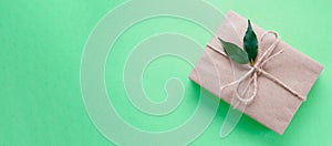 Gift box wrapped in kraft paper tied with twine decorated with green leaves on neo mint background. Color 2020. Banner
