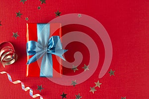 Gift box wrapped in re paper with blue ribbon on red surface. Christmas, party, birthday concept