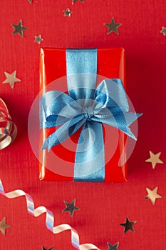 Gift box wrapped in re paper with blue ribbon on red surface. Christmas, party, birthday concept