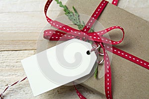Gift box, wrapped in recycled paper, red bow and tag on wood bac