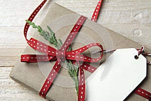 Gift box, wrapped in recycled paper, red bow and tag on wood bac