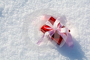 Gift box wrapped on red paper and pink ribbon with lights on snow background. Christmas and New Year holidays celebration concept