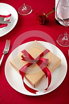 Gift box wrapped red ribbon on white plate. Romantic Valentine dinner table setting