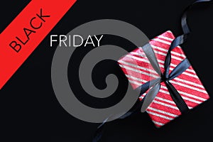 Gift box wrapped in red striped paper and tied with black bow on black background.