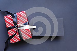 Gift box wrapped in red striped paper and tied with black bow and black tags.