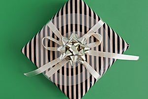 Gift box wrapped in stripped craft paper with yellow ribbon and golden bow on green background