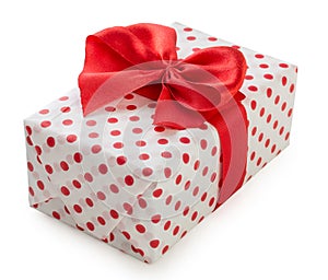 Gift box wrapped in white paper with red dots and bright red ribbon bow isolated on a white background