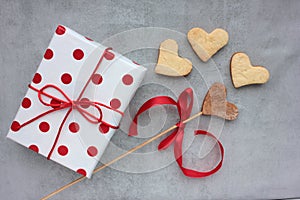 Gift box in wrapping paper with red polka dot pattern and heart shaped cookies on gray concrete background.