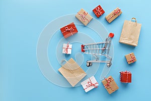 Gift boxes and bags around a shopping cart on blue background